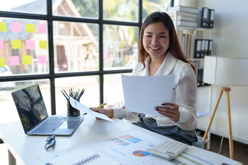 Asian female financial officer or accountant checking Calculate investment results in financial documents to report to the meeting Audit concept and investment results.