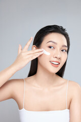 Beauty portrait image of pretty asian woman smiling and applying face cream isolated over light grey background