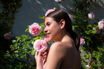 Beautiful young woman posing near roses in a spring garden. Candid lifestyle portrait of happy young beautiful sexy woman enjoying life outdoor in park at spring. Smiling girl with perfect clear skin.