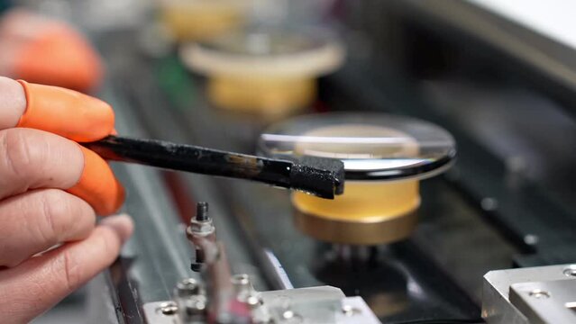 A close-up of a worker drawing black ink on the edge of the glass. Cinema lenses production. Manufacturing, industrial and technology concept.