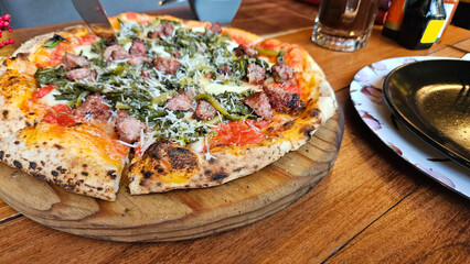 Pizza made with a circular flat wheat flour dough topped with tomato sauce and Italian sausage baked in a wood-fired oven
