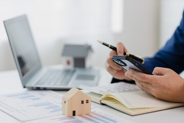 Fototapeta premium Man in a suit doing property tax calculations using a calculator of a house model