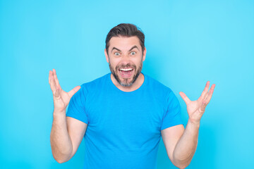 Surprised excited shocked face of millennial man isolated on studio background. Handsome happy young man showing winner gesture. Successful man with arms open. Shocked excited guy raise hands.