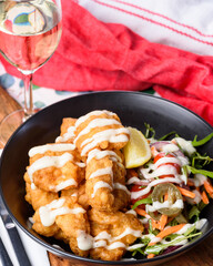A serving of deep-fried fish pieces with a white sauce and salad to the side.
