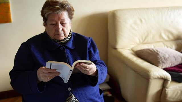 Grandmother reading a book with difficulty turning pages due to Parkinson's in her hand