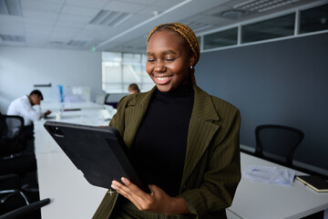 Young businesswoman in businesswear smiling and holding digital tablet while sitting on desk in office - 762955177