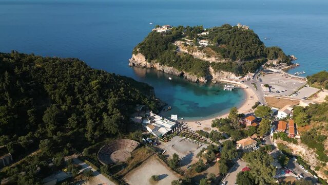 Fast aerial pan establishes protected sandy cove and beach with boats at dock and people relaxing in Corfu Greece