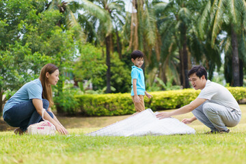 Happy cheerful Asian family with father, mother, and little son enjoy picnic together in a weekend at a park.