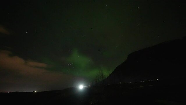 Flickering Aurora Borealis with driving cars ion road at night in Iceland Island. Wide shot.
