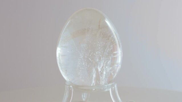 Clear Quarts Crystal mineral egg rotating on a turn table in front of a white background
