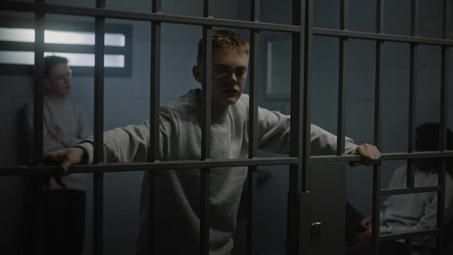 Portrait of diverse teenage prisoners behind metal bars in prison cell looking at camera. Multiethnic young inmates serve imprisonment terms in jail. Juvenile detention center or correctional facility