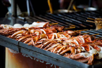  fresh squids is being grilled to a golden perfection on the barbecue grill - obrazy, fototapety, plakaty