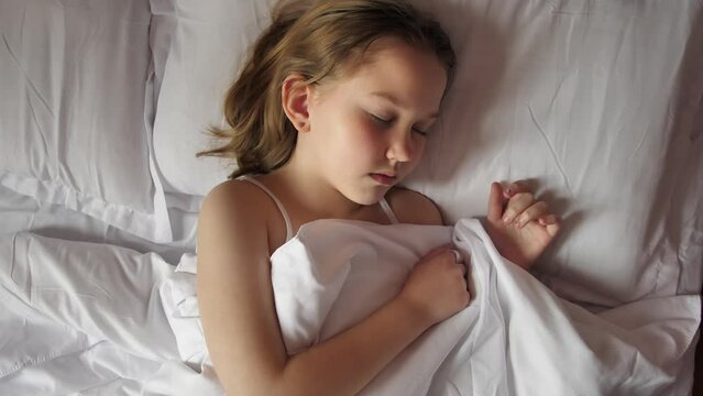 Top view of a girl with brown hair sleeping on a bed with white linen and white pillows. Cute sleeping baby. Healthy good children's sleep. Nothing bothers the child during sleep.
