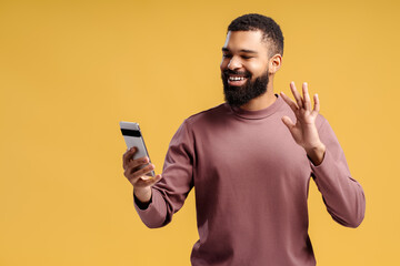 Handsome, bearded African American man, blogger holding mobile phone, using mobile app waving hand
