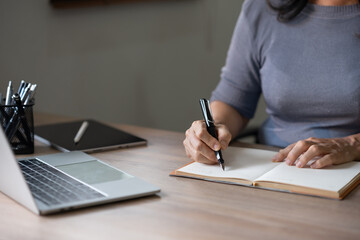 A woman is writing in a notebook while sitting at a desk