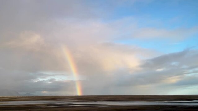 Beautiful rainbow by Icelandic plains descending from cloudscape to ground, from moving car driving by