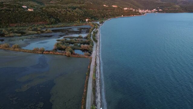 Land bridge leading through water towards main land. Aerial footage, tilted.