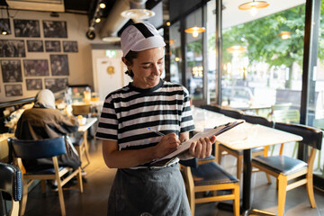 Smiling Female Chef Writing on Clipboard in Bistro