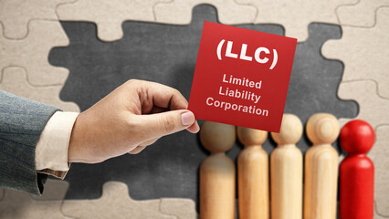 Business hand holding a note with LLC text, the acronym of Limited Liability Company with a row of wooden peg dolls - obrazy, fototapety, plakaty