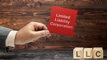 Business hand holding a note with LLC text, the acronym of Limited Liability Company with a row of...