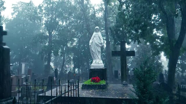An old white statue of Mary  at the Bernardine XIX century cemetery on heavy rain. Tombstones with crosses and trees in the background. Slow motion. VILNIUS, LITHUANIA - 08 15 2023.
