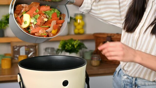 Woman throwing vegetables peels in a compost bin from a collection vessel. Housewife cooking food and composting organic waste in a bokashi container at home. Ecological and sustainability concept