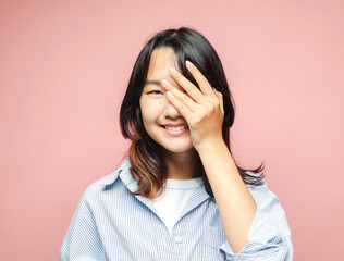 Cheerful beautiful Asian teenager laughs, covering her eyes with her hand.