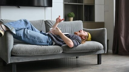 A guy is lounging on the couch at home and throwing corn sticks into the air to catch them in his mouth.