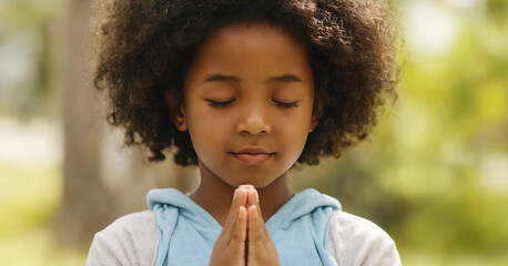 Young african girl with closed eyes, praying and expressing her faith with innocence and hope. - obrazy, fototapety, plakaty