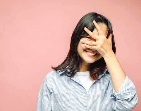 Cheerful beautiful Asian teenager laughs, covering her eyes with her hand.