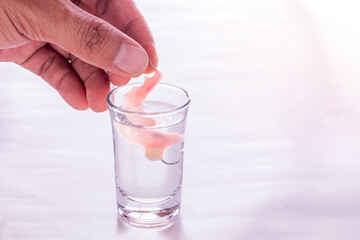Close up hand hold a acrylic dentures immersed in a glass of water