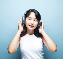 Pretty smiling Asian teenage girl listens to music on headphones over blue background.