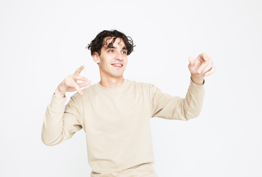 A cheerful young man in a beige sweater dances on a white studio background, enjoys life