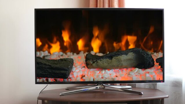 Video of a blazing fireplace on a large TV screen in an apartment. The image of the fireplace on the monitor display. Calming fire background screensaver for relaxation. Looped video.