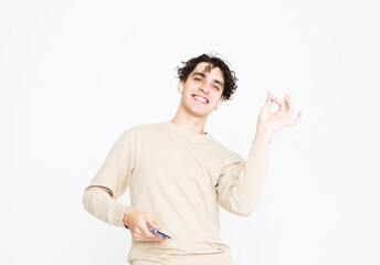 A cheerful young man in a beige sweater dances on a white studio background, enjoys life