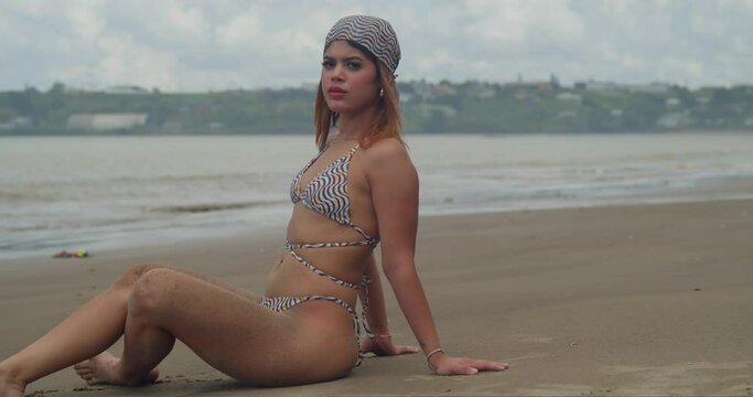 A bikini-clad Hispanic woman relishes her time sitting at a beach on a tropical Caribbean island.