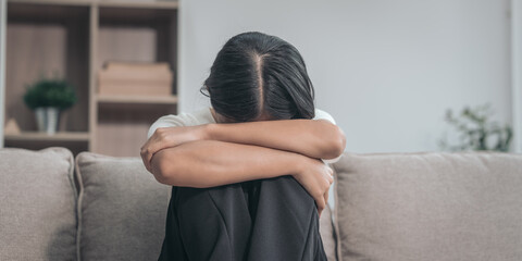 Young Asian woman sitting on sofa, depression, distressed, touches face and head, eyes closed....