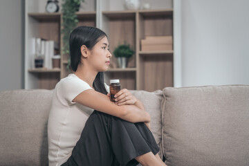 Young Asian woman sitting on sofa, depression, distressed, touches face and head, eyes closed. tired, sick, and stressed, possibly grappling with bad news or crisis, experiencing headache or migraine