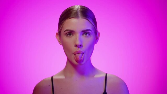 Naughty young woman sticks out tongue, looking at camera, studio shot, purple