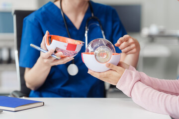 Female Caucasian ophthalmologist explains about eye diseases using the eye model with an Asian...