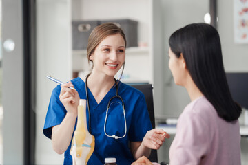 Caucasian female doctor explain to asian female patient using knee bone model at desk in medical...