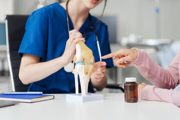 Caucasian female doctor explain to asian female patient using knee bone model at desk in medical...