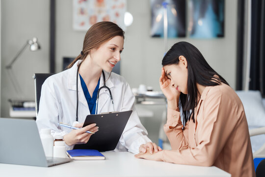 Attractive female Caucasian female doctor and psychologist gives advice, encouragement to female Asian patients. from depression in hospital examination room. cognitive behavioral therapy CBT