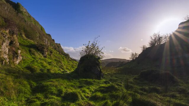 Timelapse of rural nature grassland with single rock boulder in a valley with sun setting behind hill viewed from Carrowkeel in county Sligo in Ireland.