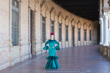Young and beautiful woman with typical green dress with ruffles and dancing flamenco in plaza de...
