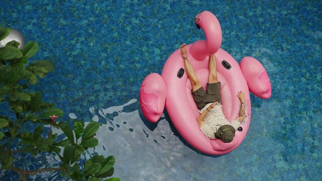 Aerial view of Man use phone on inflatable pink flamingo float mattress on pool party. 