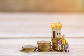 Miniature people: Businessman and family standing with step of coins and toy house.