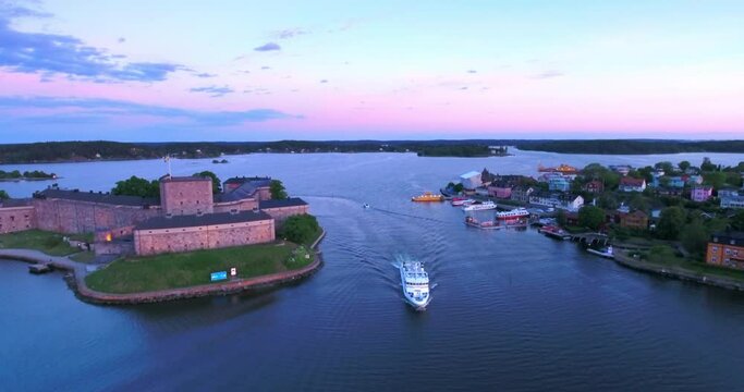 Aerial: The Ancient Stone Fortress Stands Guard At The Water'S Edge, Its Historical Significance Lingering In The Quiet Dusk, As A Modern Vessel Glides By - Stockholm, Sweden