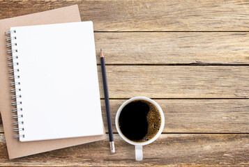Blank paper notebook,pencil and coffee on brown wooden table background.