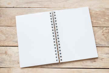 Blank paper notebook on brown wooden table background. Top view with copy space (selective focus).